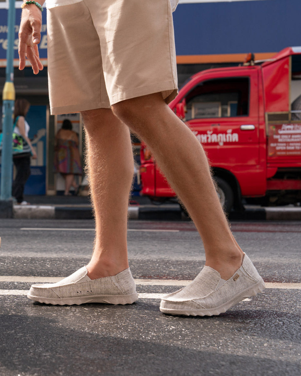 Person wearing light-colored slip-on shoes and beige shorts on a street with a red truck in the background.